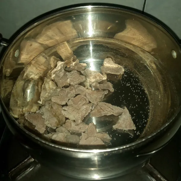 Rebus daging sampai keluar busa kotornya. Buang air rebusan pertamanya dan bilas daging hingga bersih. Rebus kembali daging dengan 700 ml air dengan api kecil.