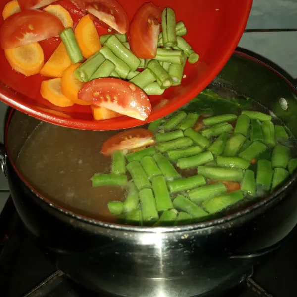 Masukkan wortel, buncis dan sebagian tomat. Bumbui garam dan kaldu sapi bubuk. Masak sayuran setengah matang.