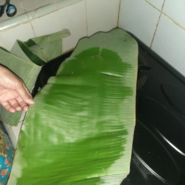 Siapkan daun pisang dengan memanaskannya di atas api kompor agar tidak mudah robek.