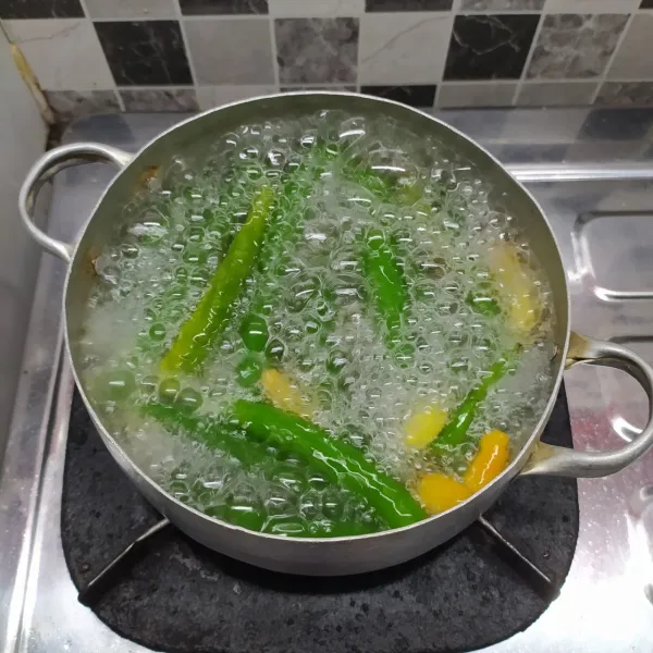 Rebus air sampai mendidih. Masukkan cabai hijau, cabai rawit, tomat, bawang merah, bawang putih dan kemiri. Rebus selama 10 menit lalu angkat dan tiriskan.