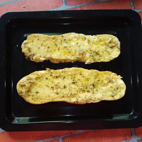 Belah baguette yang sudah dipanggang sebelumnya menjadi 2, olesi dengan garlic butter hingga merata.