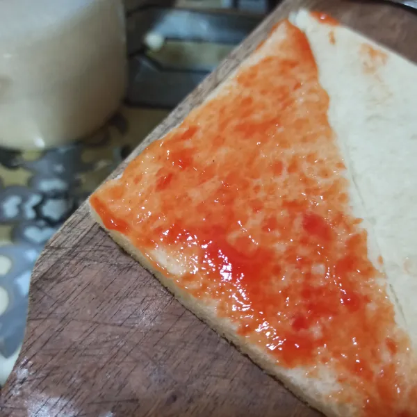 Siapkan roti bagi jadi 2 bagian (menyerong). Olesi dengan saos tomat.