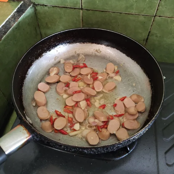 Tumis bawang merah, bawang putih, cabai merah, dan sosis hingga harum dan matang.