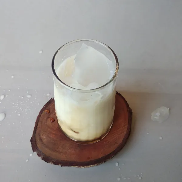 Tuang susu kedalam gelas berisi gula aren dan es batu.