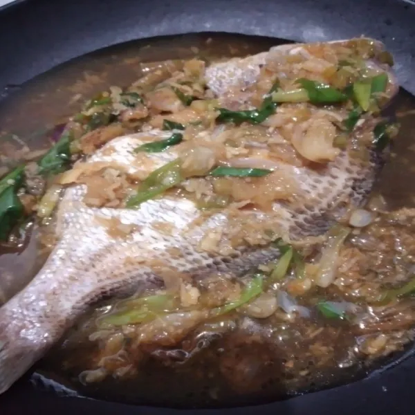Tata ikan pada piring saji, siram dengan kuahnya, taburi potongan daun bawang segar di atas ikan, siap disajikan