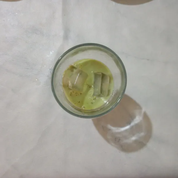 Dalam gelas saji masukkan es batu dan larutan greentea.