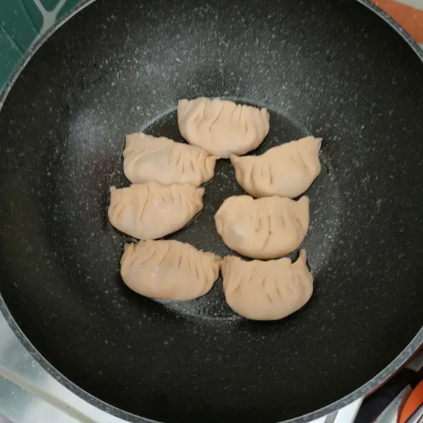 Olesi wajan anti lengket dengan minyak goreng, tata jiaozi, masak hingga sisi bagian bawah berwarna kecoklatan.