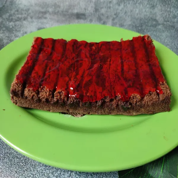 olesi bagian atas cake coklat dengan selai strawberry.