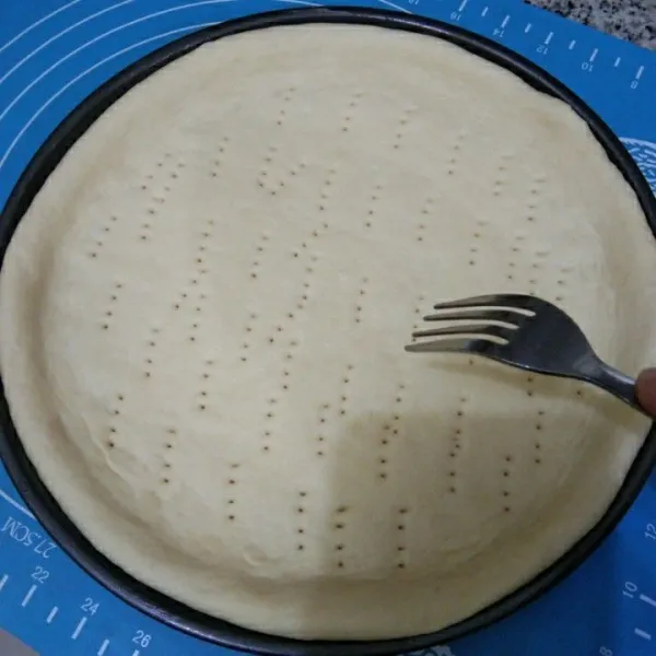 Tipiskan adonan pizza menggunakan rolling pin, lalu bentuk bulat. Siapkan loyang yang telah diolesi margarin, kemudian tata adonan, lalu tusuk-tusuk adonan menggunakan garpu.