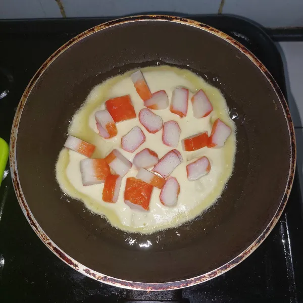 Oles sedikit minyak goreng, tuang 1/3 adonan lalu bentuk menjadi lingkaran lalu tabur potongan crabstick di atasnya.
