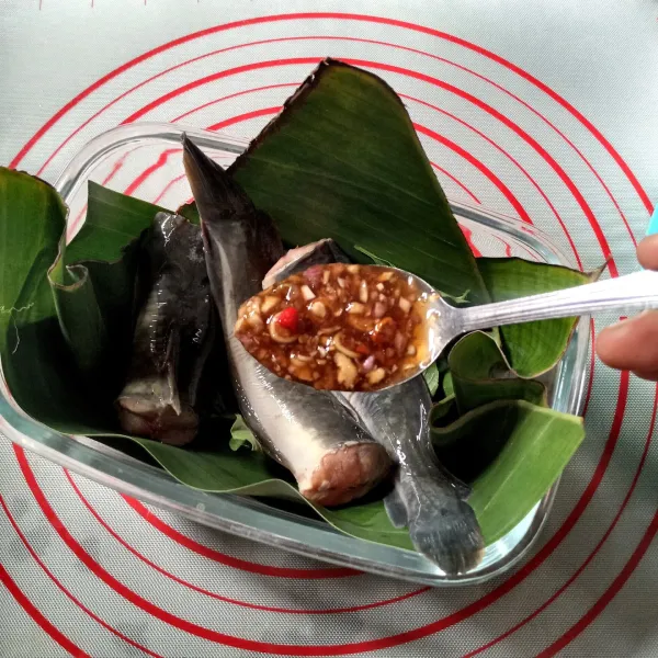 Siapkan pingga tahan panas, alasi dengan daun pisang. Tata sebagian kemangi didasar lalu timpa dengan ikan lele. Beri saus merata.