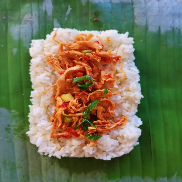 Siapkan daun pisang, lalu tambahkan nasi dan taburkan ayam di atasnya.