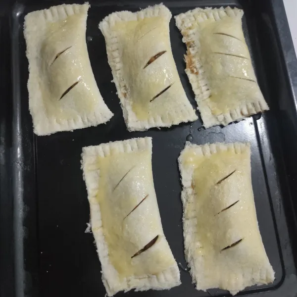 Tata dalam loyang, roti yang sudah dilipat. Lalu olesi dengan kuning telur.