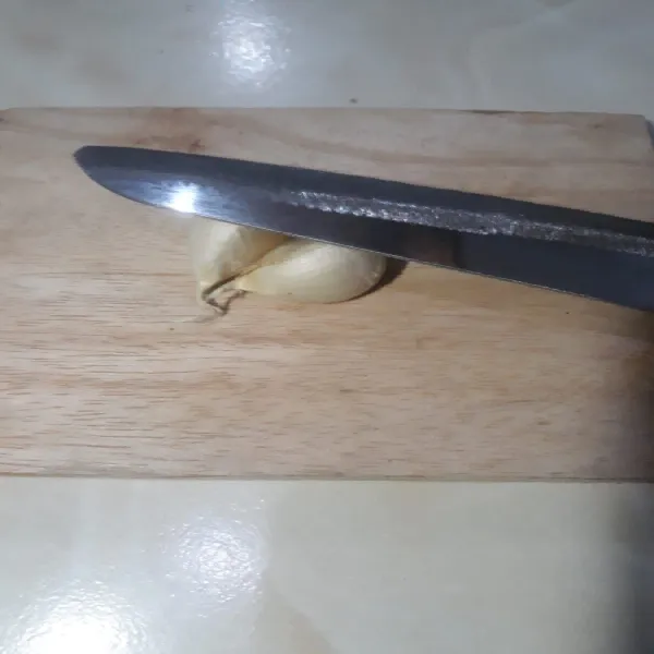 Letakkan pisau dapur di atas bawang putih.pastikan semua bawang putih di bawah pisau
