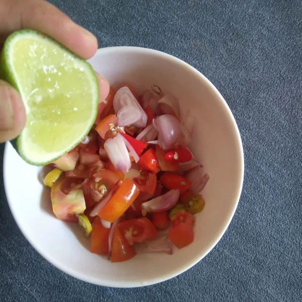 Pindahkan irisan tomat, bawang merah, dan cabe rawit ke dalam mangkuk. Tambahkan air perasan jeruk nipis.