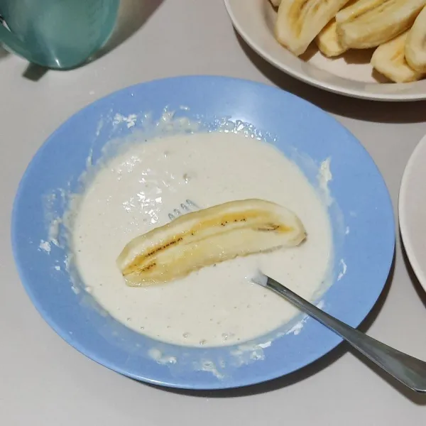 Lalu belah pisang menjadi 2 bagian kemudian celupkan di adonan tepung.
