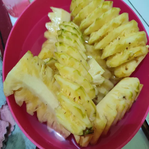 Potong nanas menjadi beberapa bagian, rendam dengan air garam agar nanas tidak gatal di mulut.