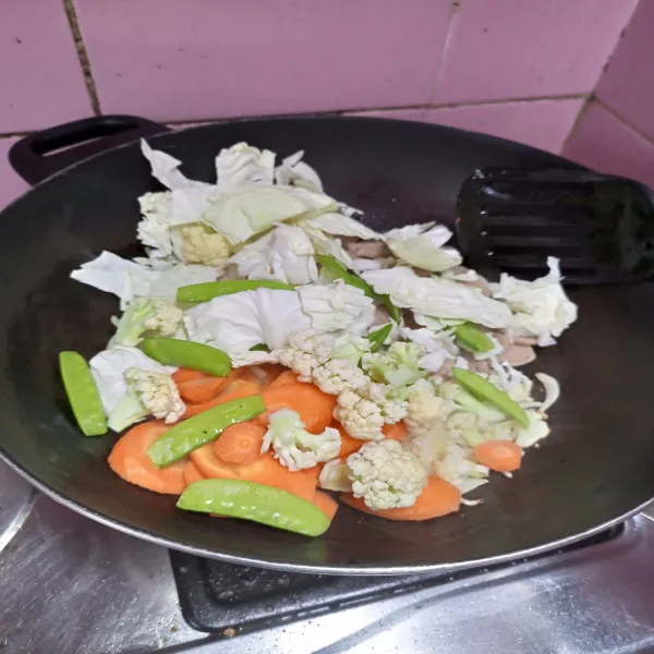 Tambahkan kembang kol, kol, wortel, kapri, tomat dan bakso. Tumis sampai sayuran layu.