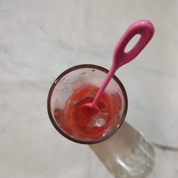 Siapkan gelas saji, tempelkan selai strawberry di dinding gelas.