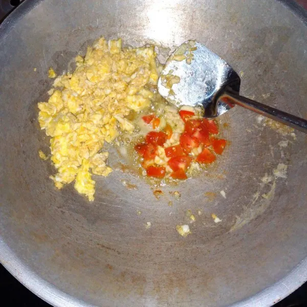 Sisihkan telur ke pinggir wajan, tuang sedikit minyak lagi, lalu masukkan bawang putih, cabai rawit, dan tomat. Tumis hingga harum.