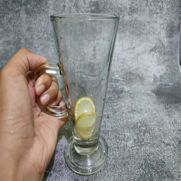Masukkan lemon ke dalam gelas saji, kemudian beri es batu.