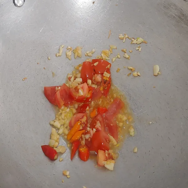 Panaskan 3 sdm minyak untuk menumis, tumis bawang putih hingga layu.
Masukkan tomat dan cabai merah, aduk rata.