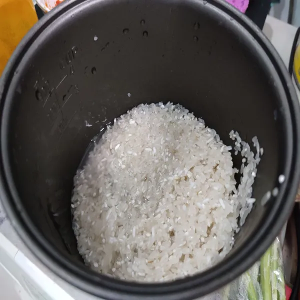 Cuci bersih beras, pindahkan ke dalam panci rice cooker.