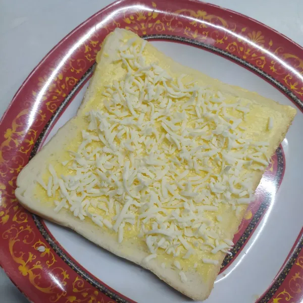 Roti pertama oles kedua sisi dengan margarin. 
Beri salah satu sisi dengan keju parut.