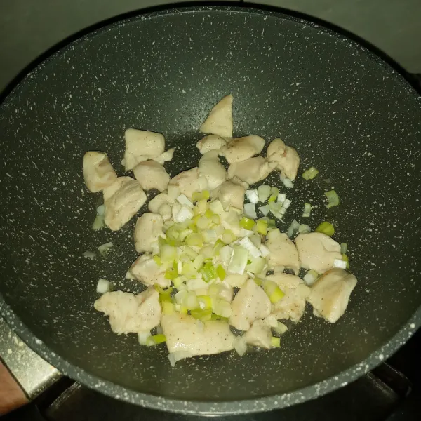 Panaskan wajan anti lengket. Tumis ayam sampai berubah warna. Masukkan daun bawang bagian putih yang dicincang. Tumis sampai layu.