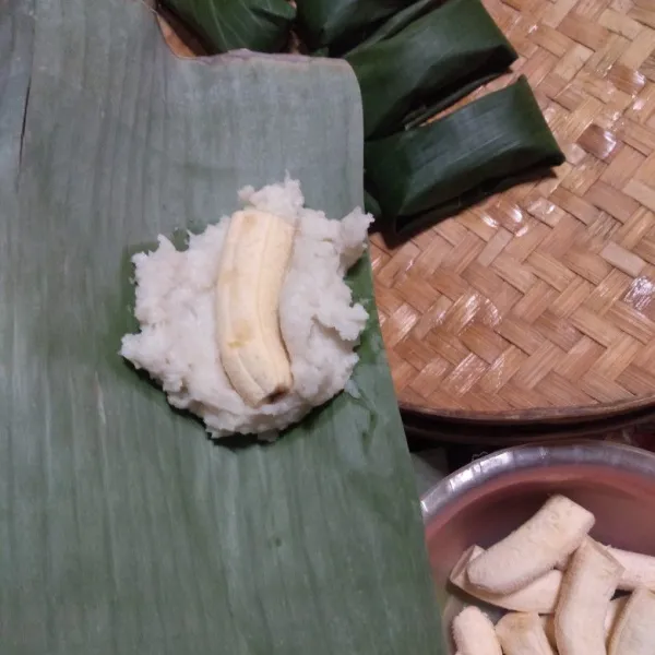 Ambil adonan secukupnya dan letakkan di atas daun pisang, beri sepotong pisang di atasnya dan rapikan hingga pisang tertutup adonan.