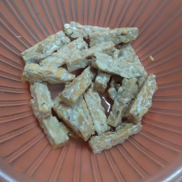 Iris panjang tempe berbentuk stick, lalu baluri tempe dengan garam, bawang putih bubuk, dan kaldu jamur, aduk merata. Kukus tempe selama 20 menit, kemudian sisihkan.