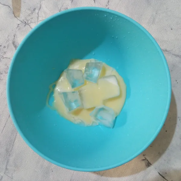 Masukkan es batu dan susu kental manis putih ke dalam mangkuk.