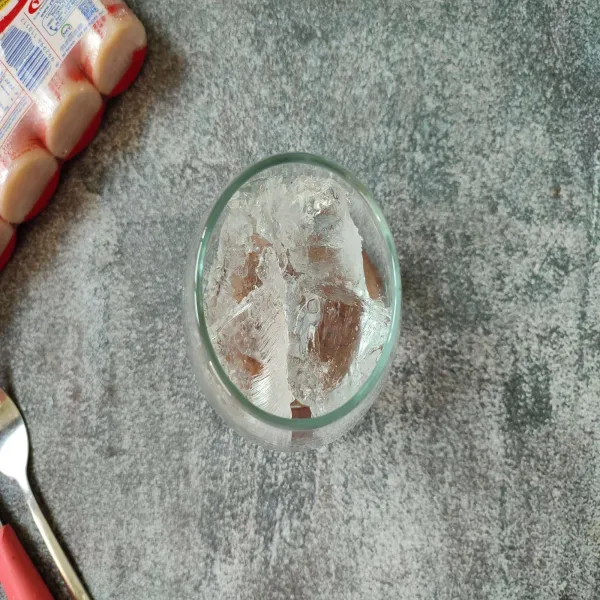 Tuangkan es batu ke dalam gelas saji.