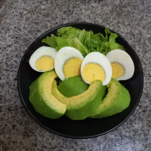 Tata potongan alpukat dan telur rebus bersama daun selada.