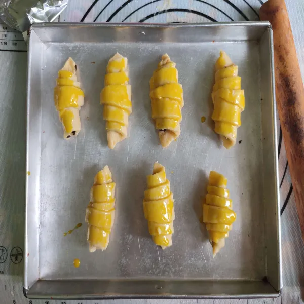 Olesi permukaan croisant dengan kuning telur.
