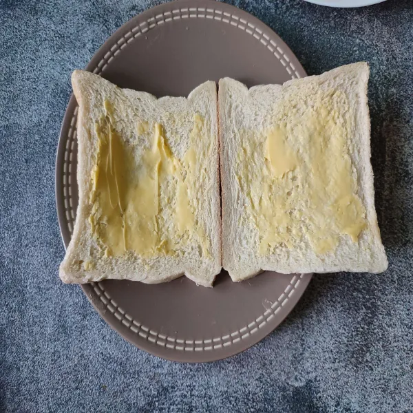 Olesi salah satu permukaan roti dengan margarin.