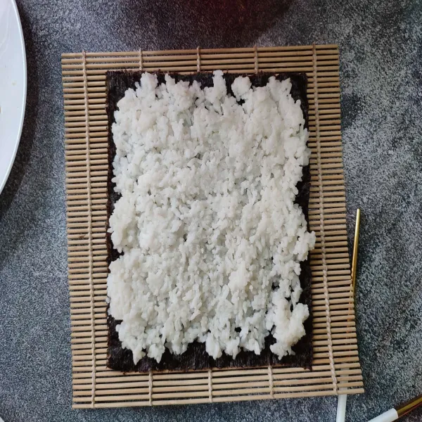 Tata nori di atas sushi matt, kemudian beri nasi putih di atasnya, ratakan.