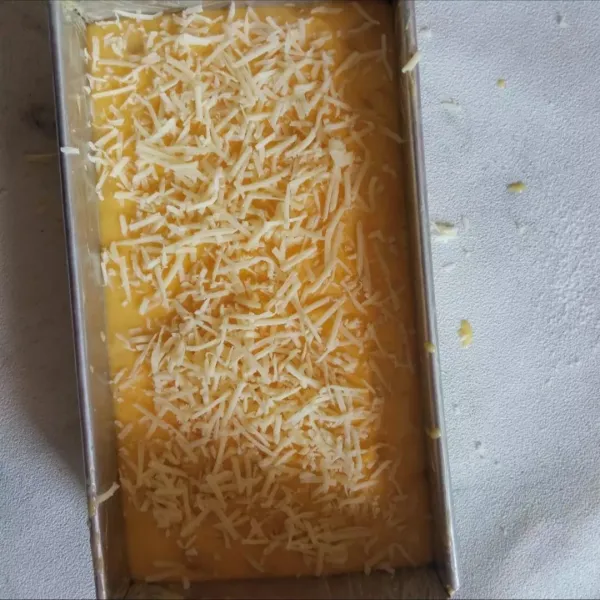 Tuang adonan ke dalam loyang yang sudah dioler margarin. 
Beri taburan keju parut di atasnya.