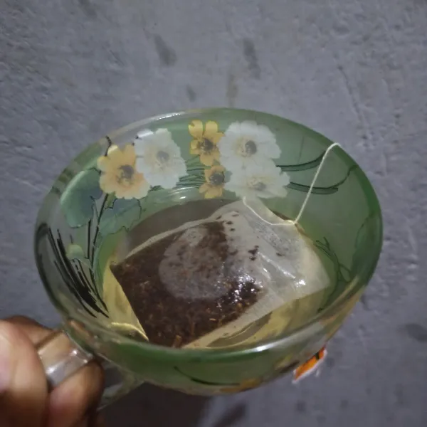 Tuang air panas perlahan di gelas yang berisi kantong teh.