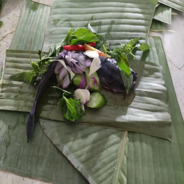Siapkan wadah daun pisang yg sudah bersih, tata ikan dengan irisan bawang, belimbing, tomat, cabe rawit, daun salam dan juga kemangi. Bungkus rapi.