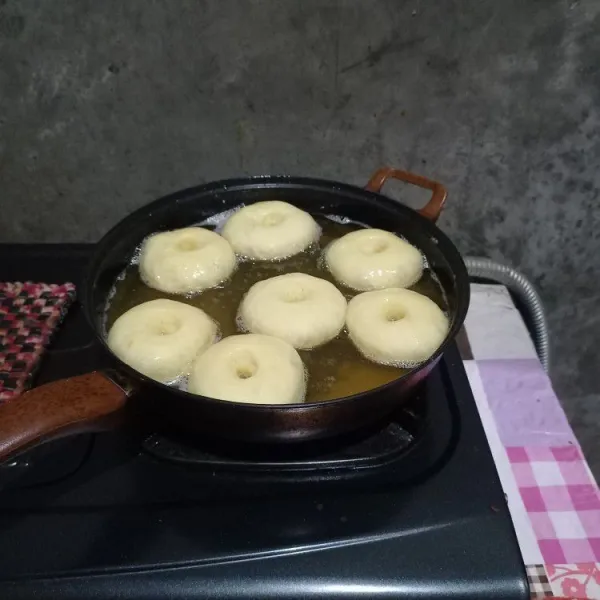 Panaskan minyak dengan api kecil sambil menunggu donat agak mengembang lagi. Kemudian goreng donat yang pertama kali dilubangi.