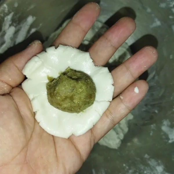 Lalu ambil adonan kulit secukupnya, pipihkan.
Beri 1 bulatan isian kacang hijau, lalu bulatkan kembali, lakukan hingga adonan habis.