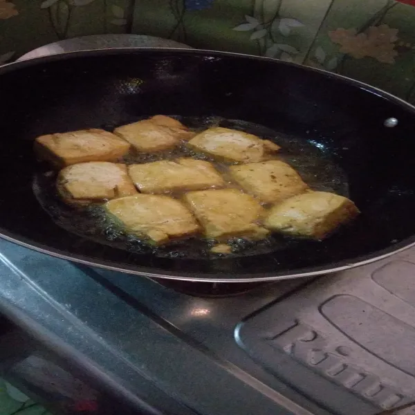 Goreng tahu sampai matang, angkat, tiriskan, setelah dingin belah tengah tidak putus.