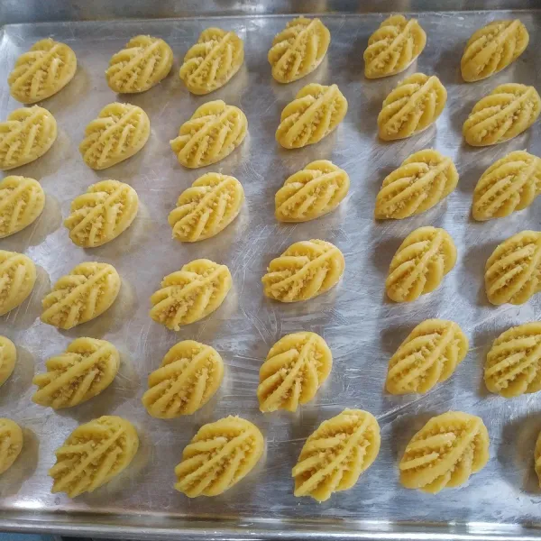 Ambil adonan sebanyak 8 gram, tambahkan selai kemudian bulatkan dan bentuk lonjong bentuk motif nastar menggunakan japitan kue.
Panggang adonan hingga hampir matang.