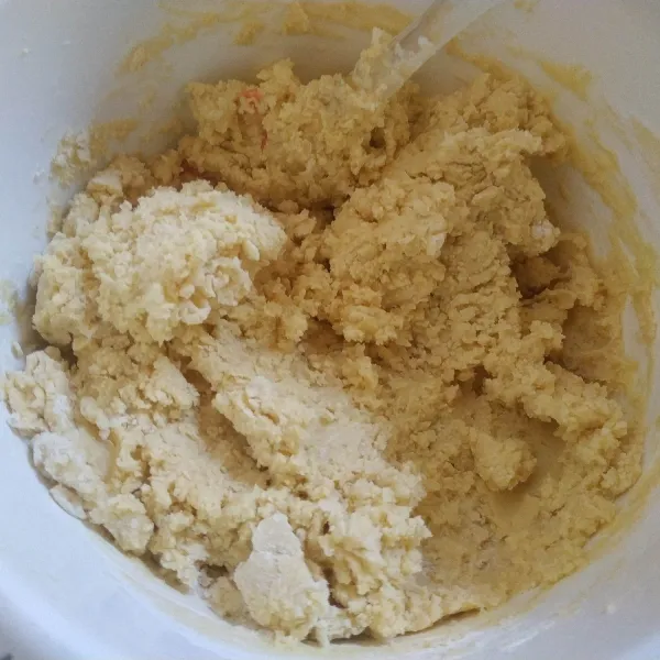 Selanjutnya masukkan vanili dan susu bubuk, aduk rata.
Tambahkan tepung terigu sedikit demi sedikit, aduk rata menggunakan spatula sampai adonan bisa dibentuk.