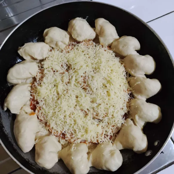 Untuk membuat pinggirannya menjadi cheesy bites, potong pinggiran kemudian putar 360° sehingga membentuk cheesy bites yang diinginkan. Kemudian oleskan saus bolognese di tengah adonan pizza, susun sosis yang telah dipotong-potong. Kemudian taburi dengan parutan keju cheddar dan mozarella diatasnya.