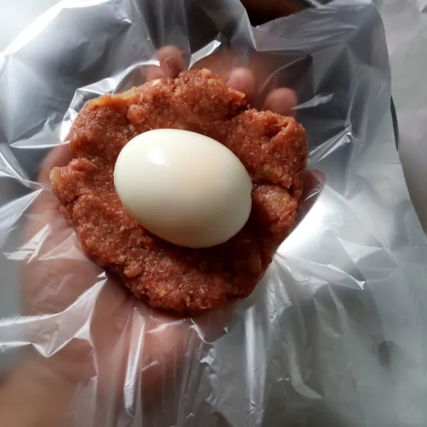 Bagi adonan daging menjadi 2 bagian sama banyak. Ambil satu bagian adonan, pipihkan. Beri telur rebus lalu bulatkan dan rapikan. Lakukan sampai selesai.