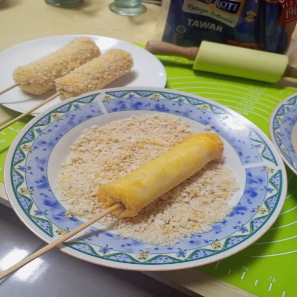 Gulingkan corndog di telur lalu gulingkan di tepung roti.