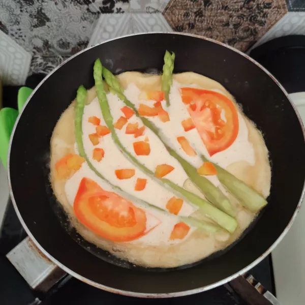 Siapkan pan anti lengket beri minyak, panaskan sebentar kemudian masukan adonan, tambahkan asparagus dan tomat.
