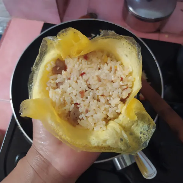 Ambil mangkuk cetakan nasi, lalu masukkan telur dadar, kemudian nasi goreng, padatkan. Lalu balik di atas piring. Kerat bagian atasnya menyilang, rapikan sehingga membentuk bunga. Kemudian garnish dan sajikan.